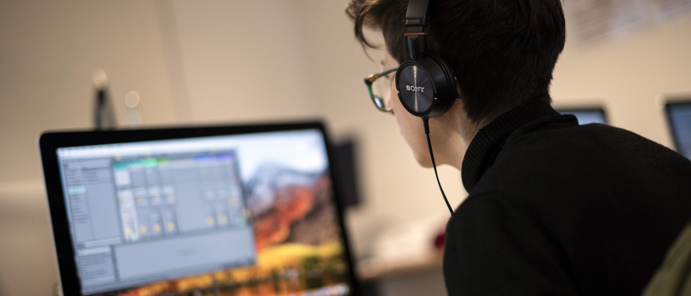 A young woman sitting at a computer using Ableton Live.