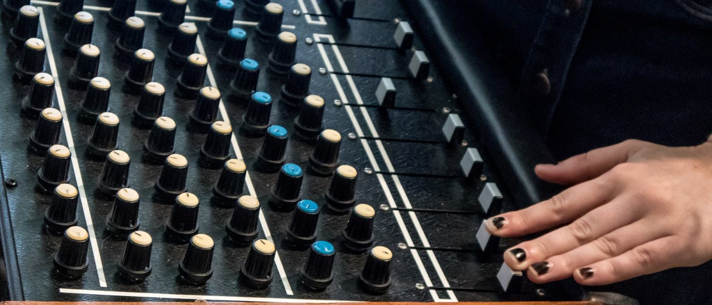 A hand wearing nail varnish operating the sliders of a large mixing desk