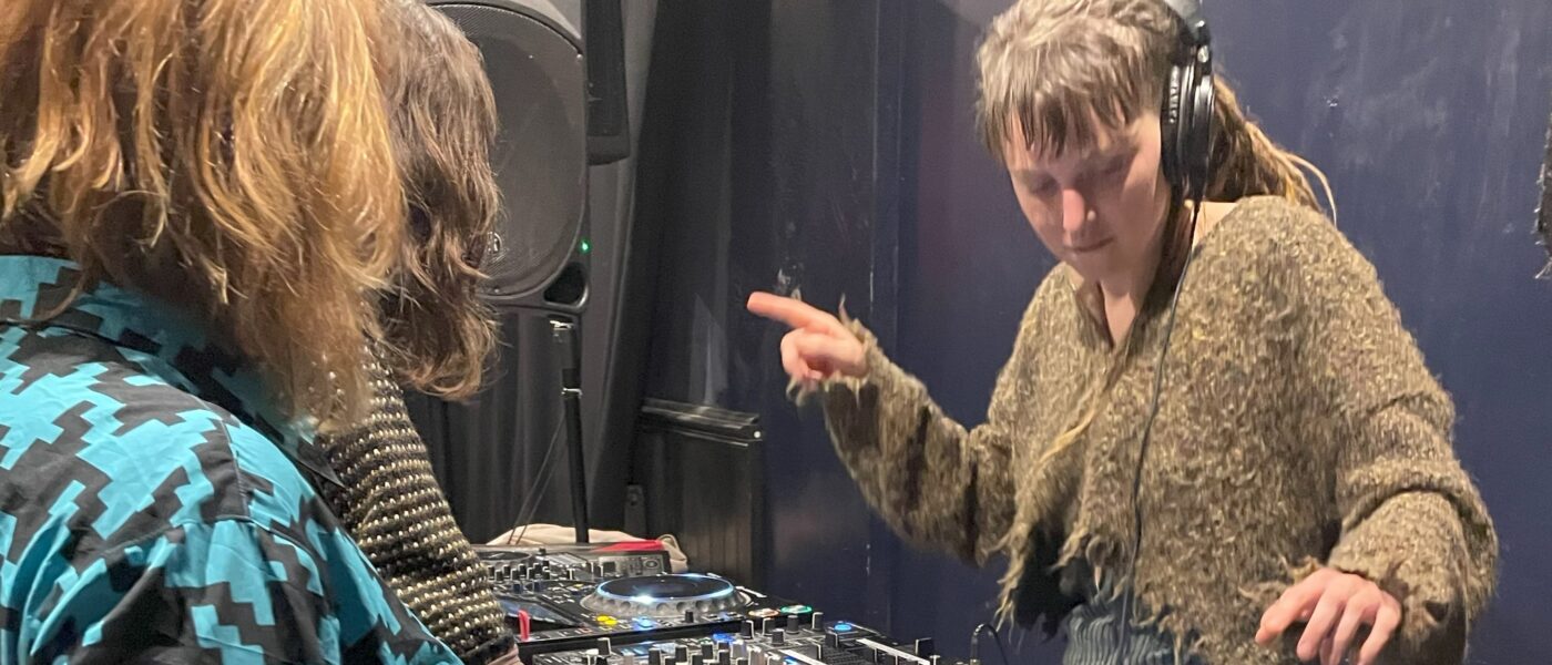 A woman dancing while she DJs, with others looking on.