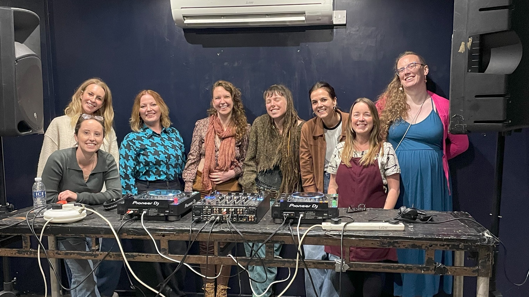 Group photo of happy Turn the Tables participants and workshop leaders standing behind a table with decks on it.
