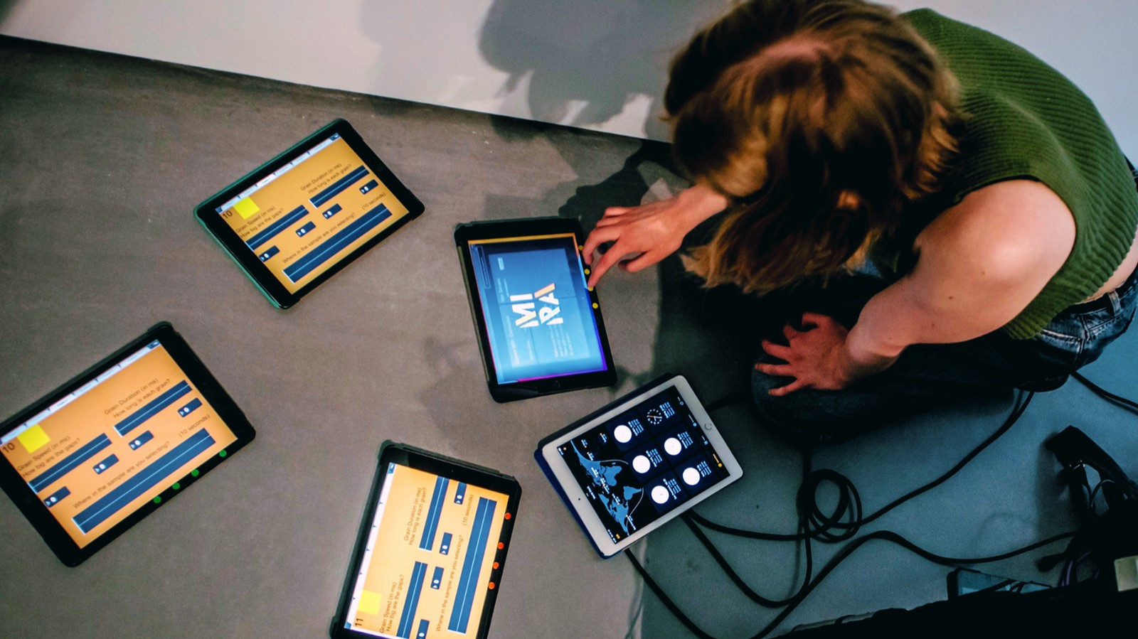 A woman photographed from above, sitting on the floor with five tablet computers running music software.